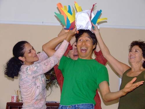 photo of 3 women holding a hat over a man's head