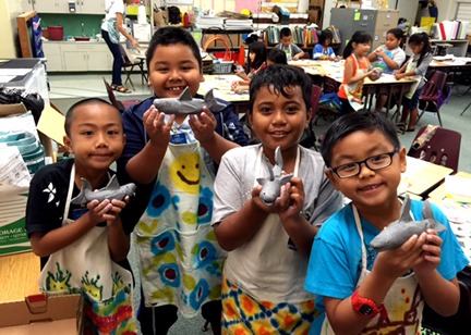 Four kids in a classroom holding up sharks