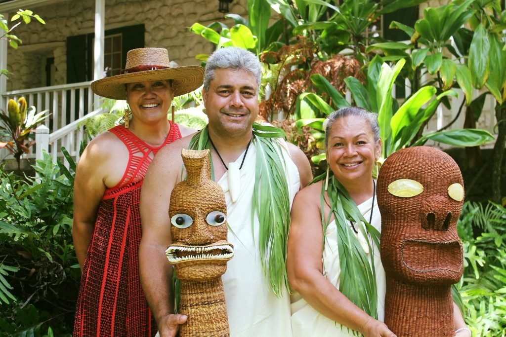 Two women and a man posing in garden holding masks