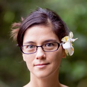 Laurel Nakanishi. Laurel is wearing glasses and there is a flower tucked behind one ear.