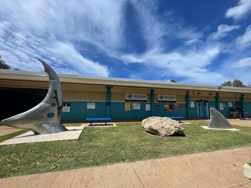Stainless steel sculpture shaped like shark fins in front of a school building