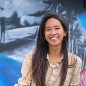 artist Sheanae Tam standing in front of a painted mural
