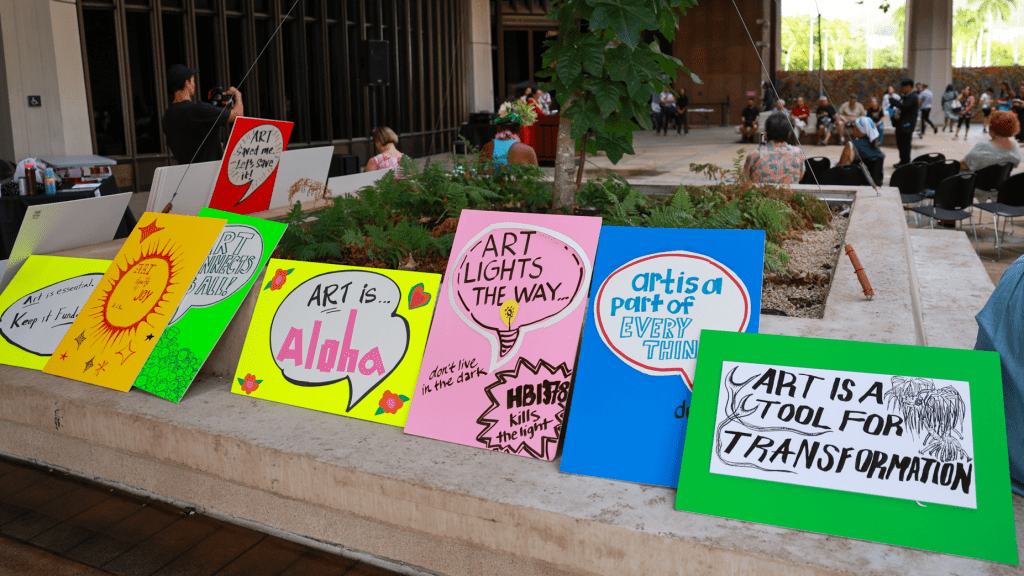A row of brightly colored handmade signs with arts advocacy slogans.